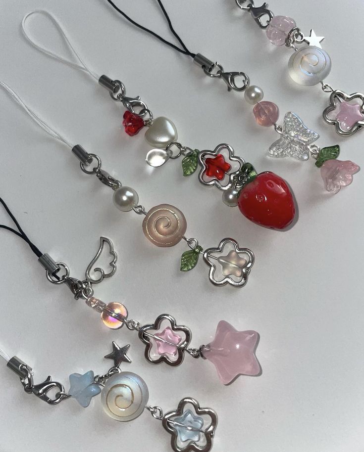 several necklaces with charms on them sitting on a white plate, one has a strawberry and the other is a star