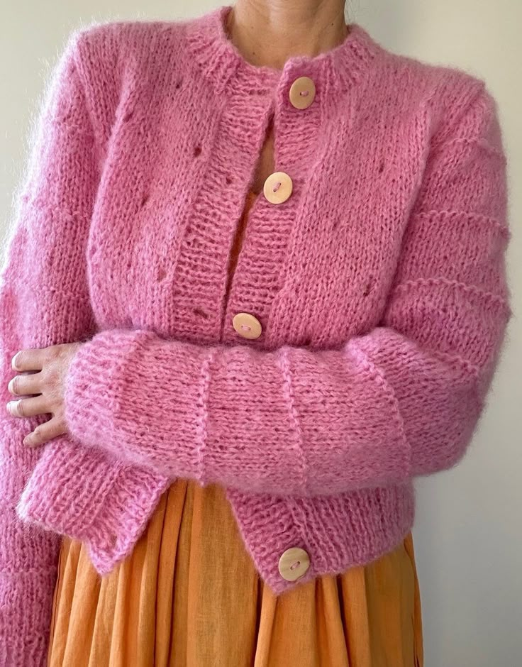 a woman wearing a pink cardigan and orange pleated skirt with her hands on her hips