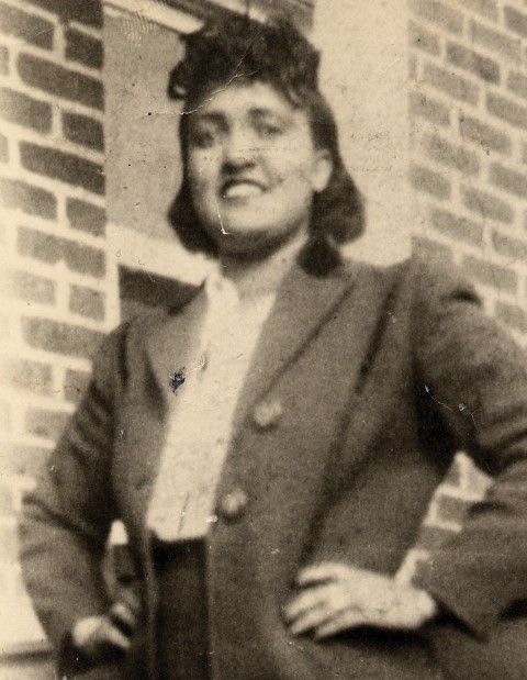 an old black and white photo of a woman standing in front of a brick building