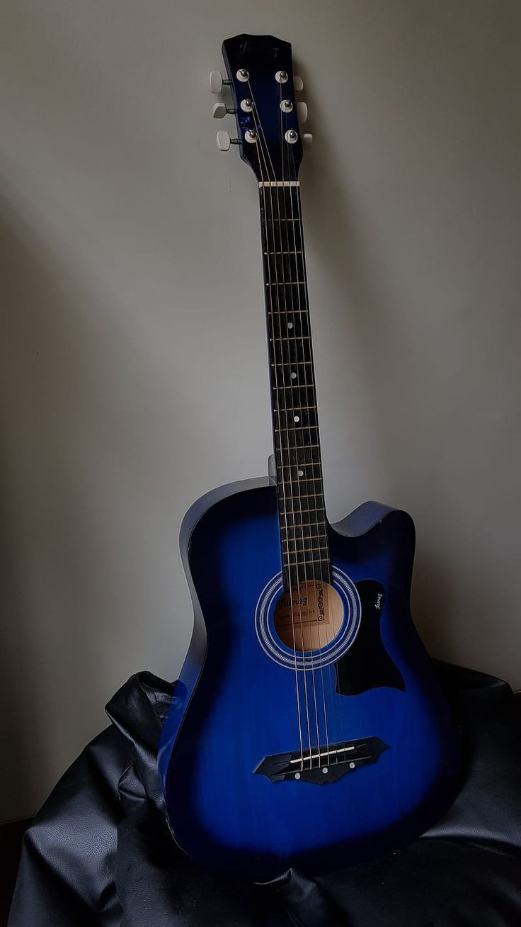 a blue acoustic guitar sitting on top of a black cloth covered table next to a white wall