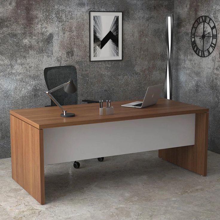 an office desk with a laptop on it in front of a gray wall and clock