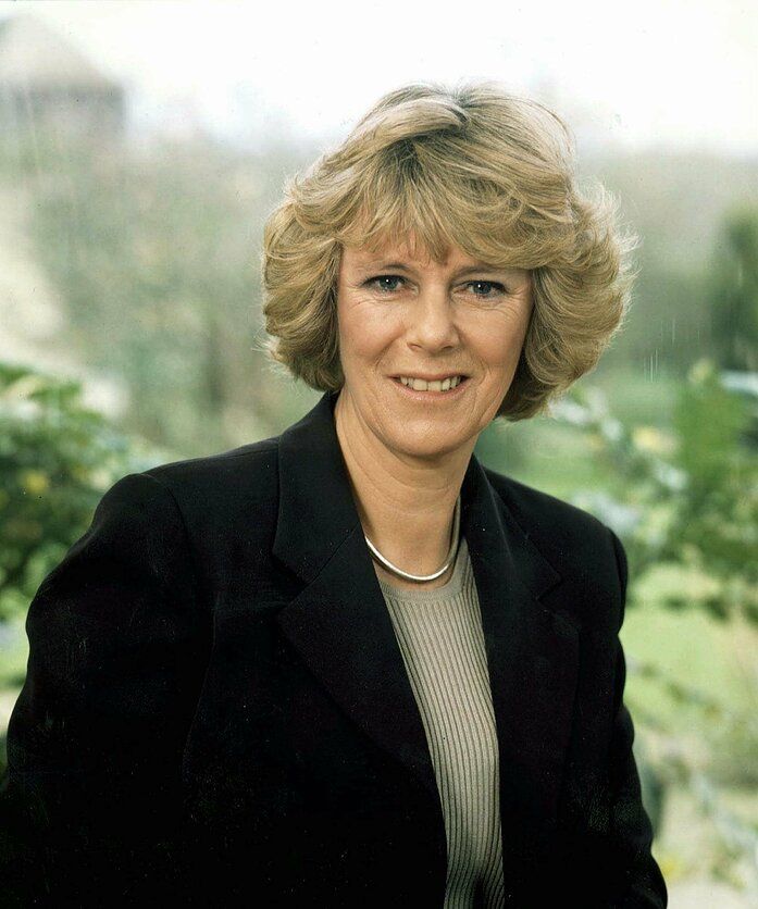 a woman in a black jacket is smiling at the camera with trees and bushes behind her