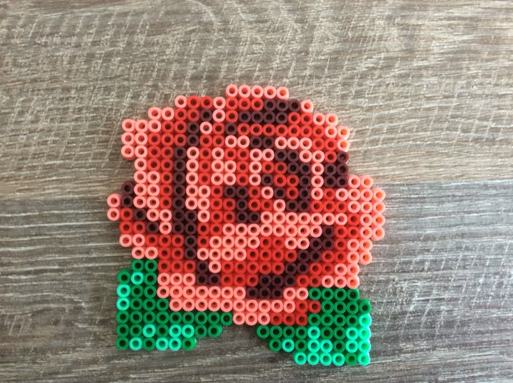 a rose made out of perler beads on a wooden surface with the word love spelled in it