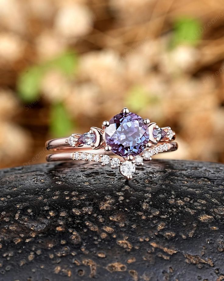 an engagement ring with two diamonds and a purple stone in the center on top of a rock