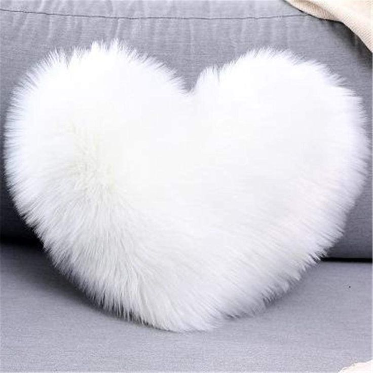 a white heart shaped pillow sitting on top of a gray couch next to a blanket