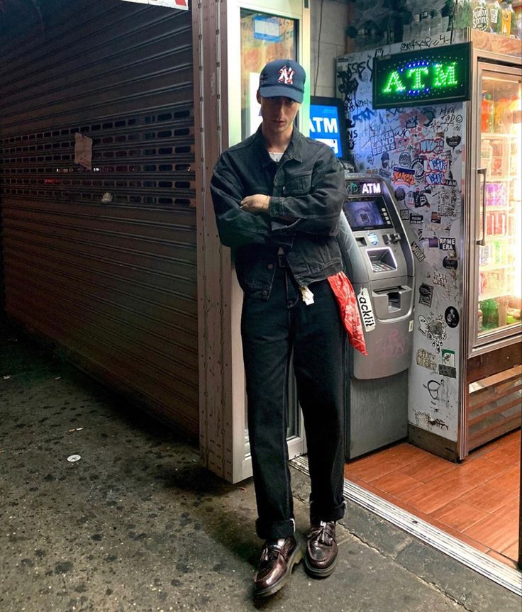 a man standing in front of a atm machine with his arms crossed and looking at the camera