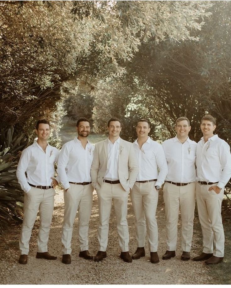 a group of men standing next to each other in front of trees and dirt ground