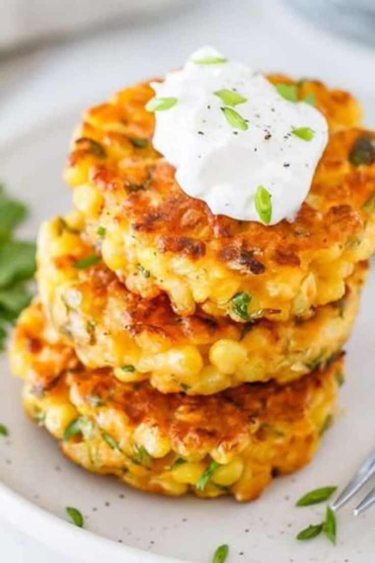 two crab cakes with sour cream on top are stacked on a white plate and garnished with parsley