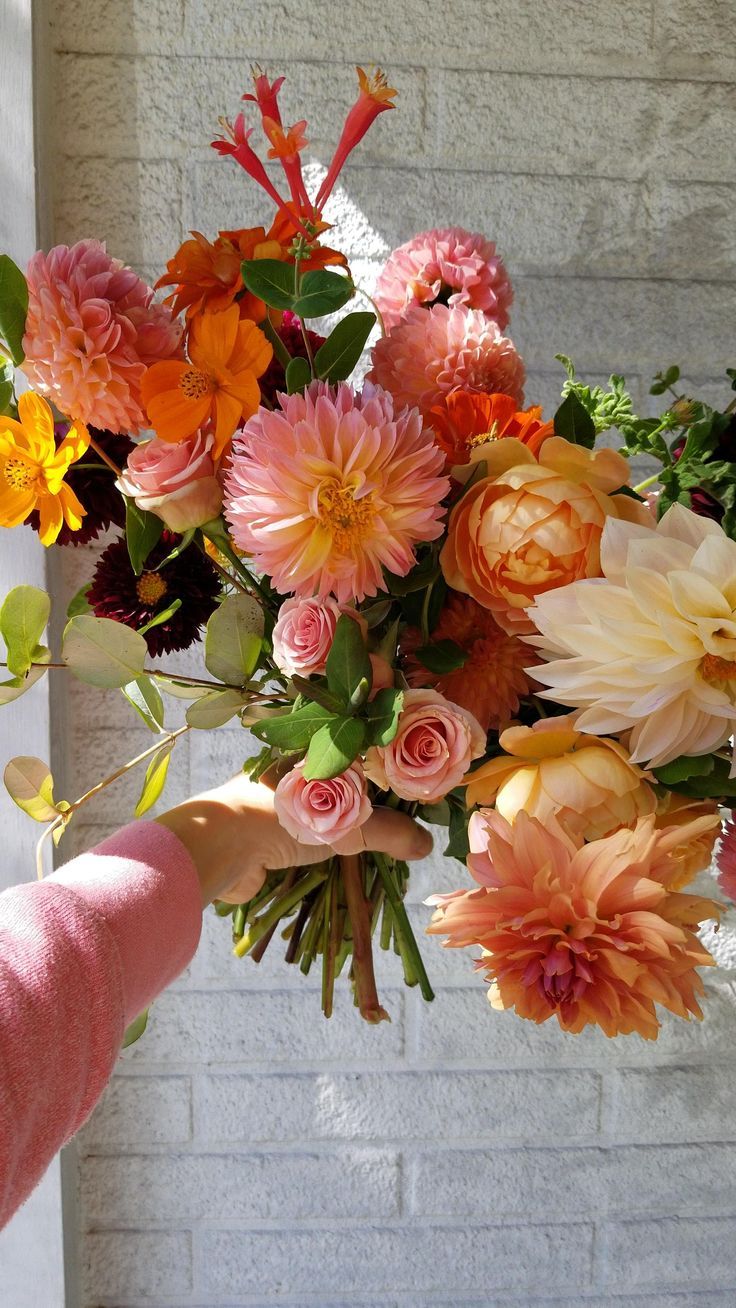 a person holding a bouquet of flowers in front of a brick wall with sunlight coming through the window