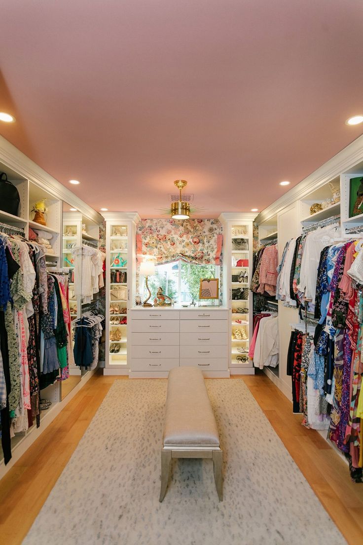 a walk in closet with lots of clothes hanging on the walls and a bench at the end