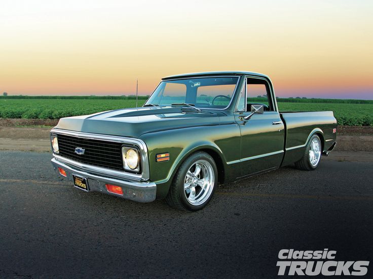 an old green truck is parked on the side of the road in front of a corn field