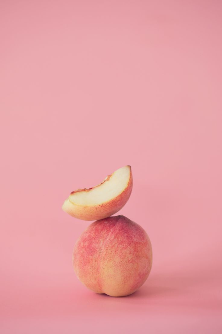 an apple is sitting on top of another apple in front of a pink background,