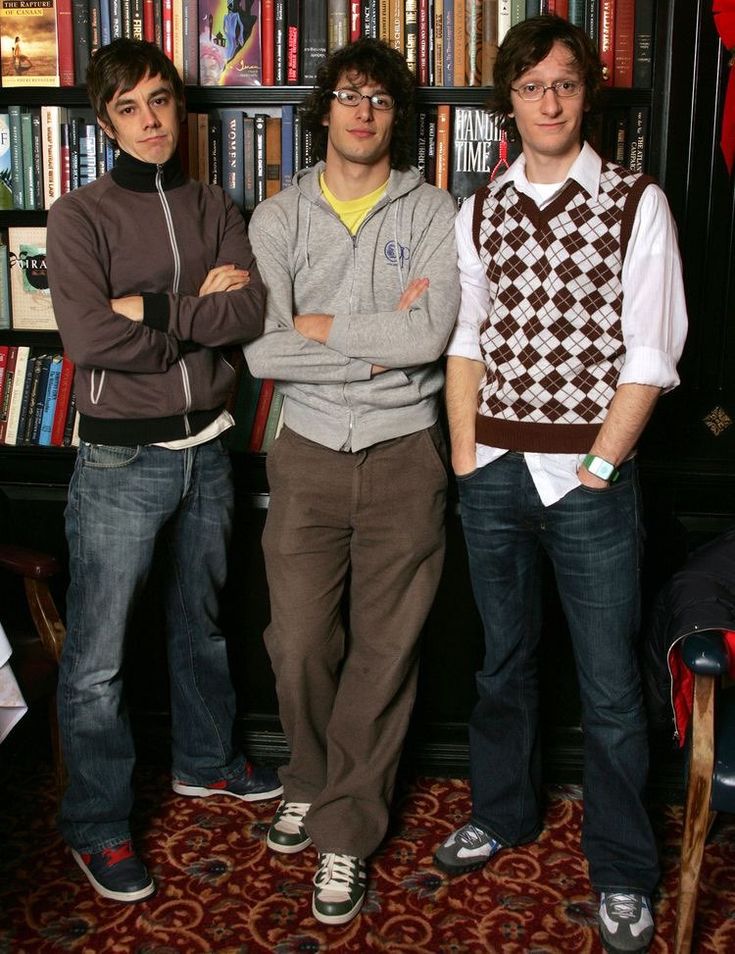 three young men standing next to each other in front of bookshelves