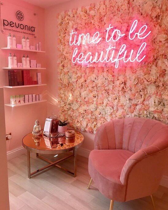 a pink chair sitting next to a table in front of a wall with flowers on it