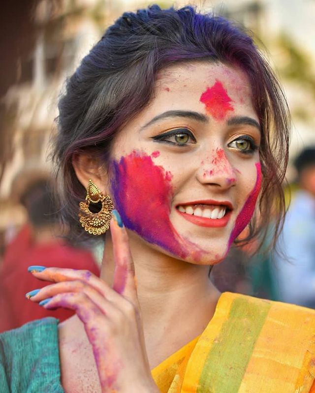 a woman with colorful paint on her face posing for the camera and holding her hand up in front of her face