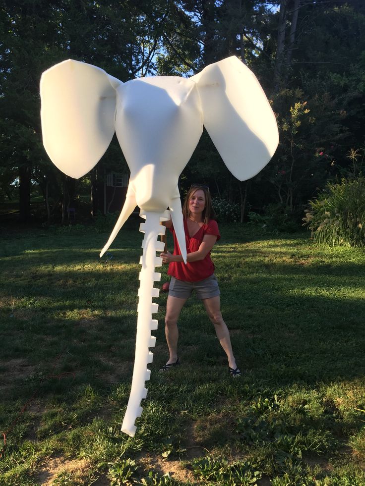 a woman standing next to a giant white balloon shaped like an elephant in the grass