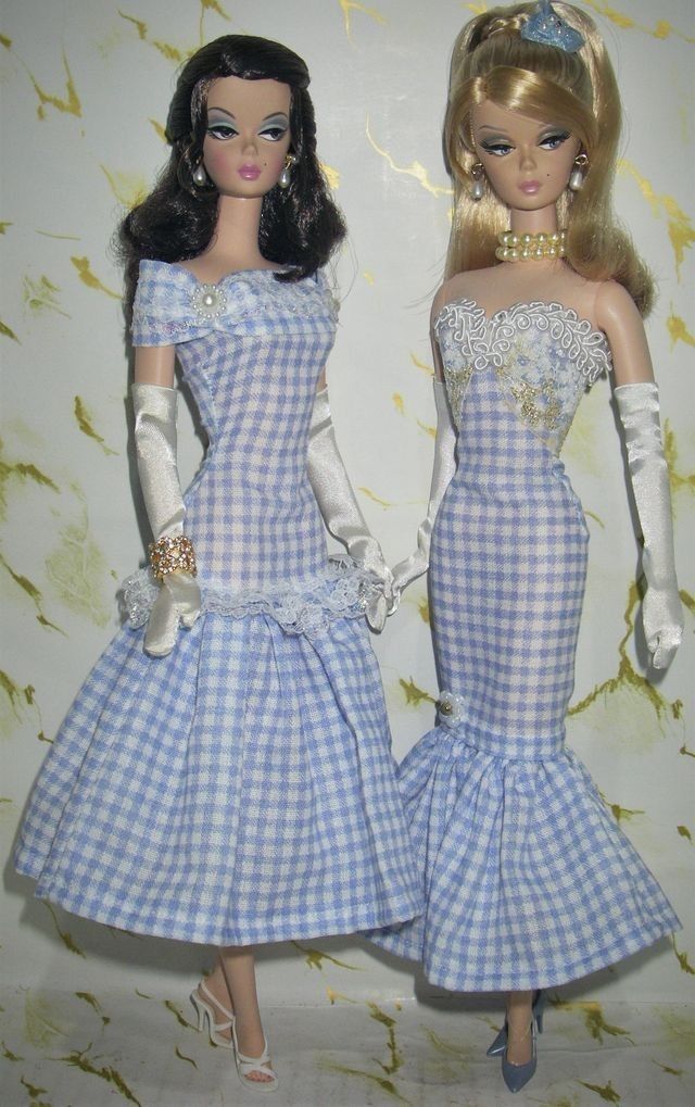 two barbie dolls are dressed in blue and white checkered dresses, one is wearing a tiara