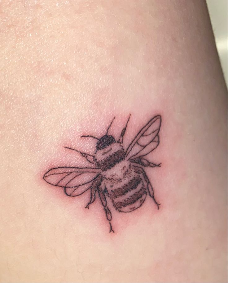 a small tattoo of a bee on the back of a woman's thigh,