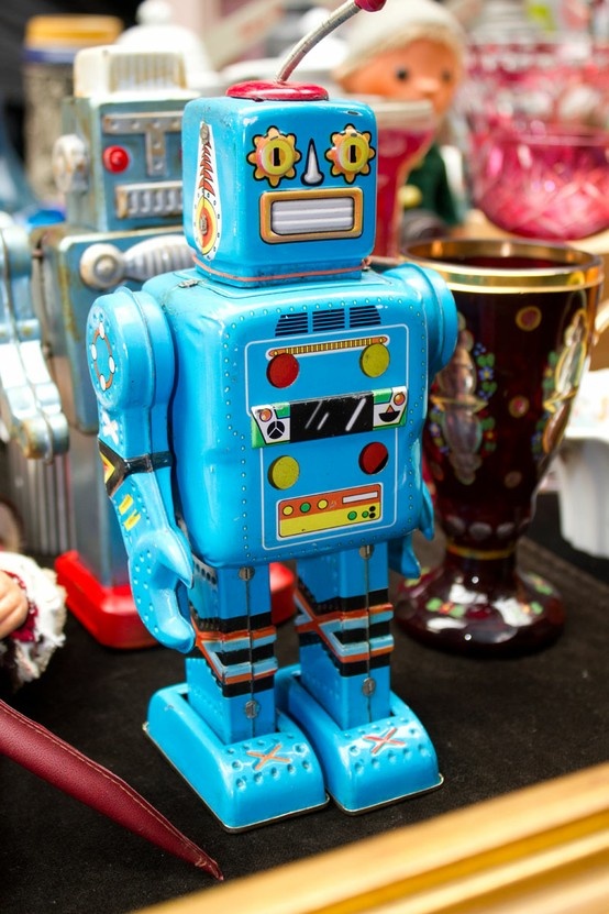 a blue toy robot sitting on top of a table next to other toys and vases