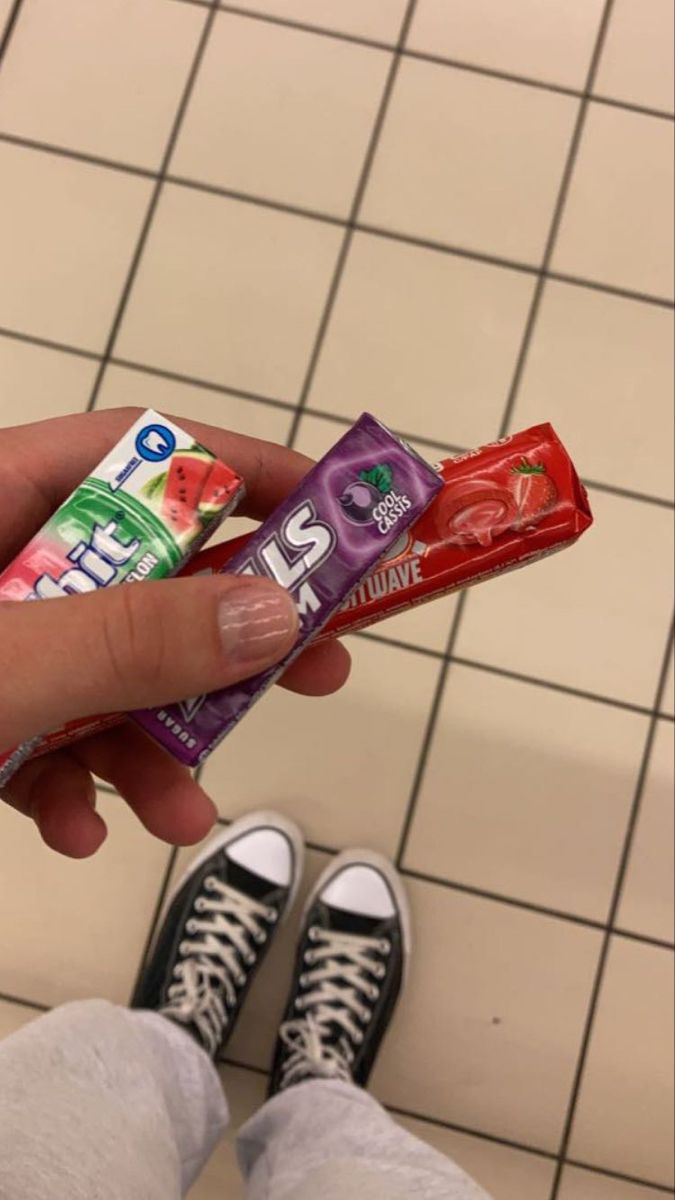 a person holding two bars of candy in their hand on a tiled floor next to shoes