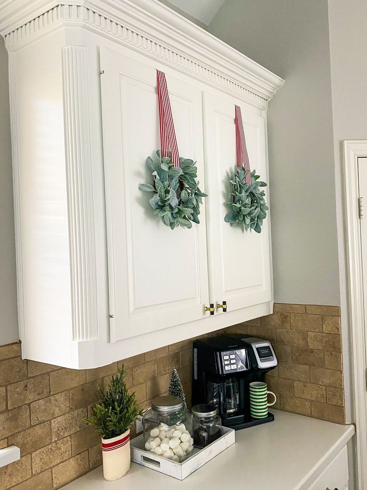 a kitchen with white cabinets and christmas wreaths on the wall over the coffee maker