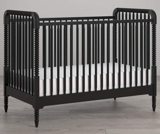 a black crib with white sheets on the bottom and side, against a gray wall