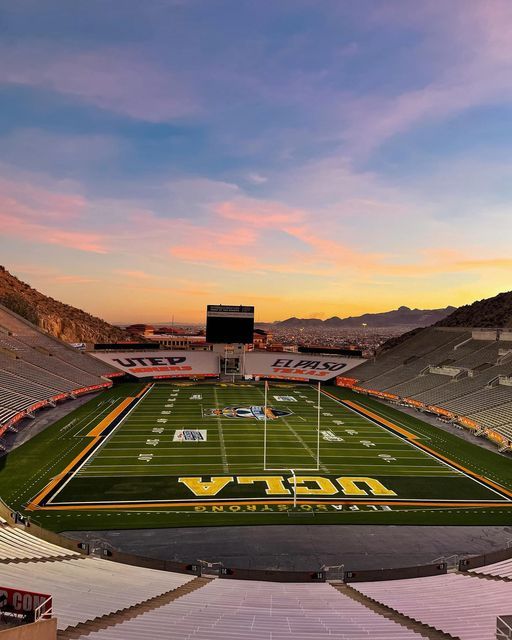 an empty football stadium at sunset with the sun going down on the field and mountains in the background