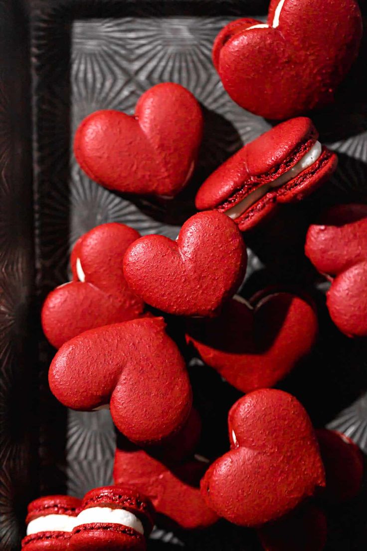 heart shaped red velvet pastries are arranged on a black and silver tray with hearts in the middle