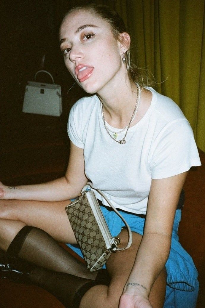 a woman sitting on the floor with her handbag in her lap and tongue out