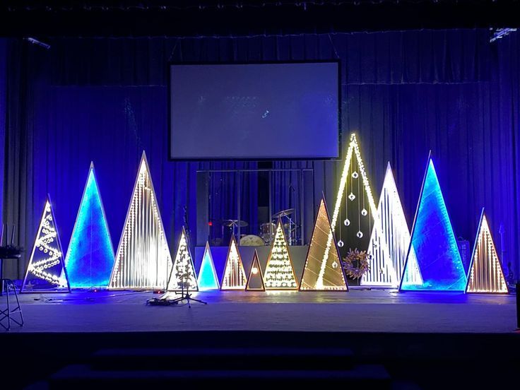 a stage set up with christmas trees on it and a projector screen in the background