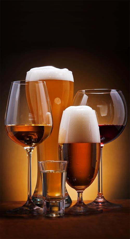 three glasses of different types of wine and beer on a wooden table with brown background