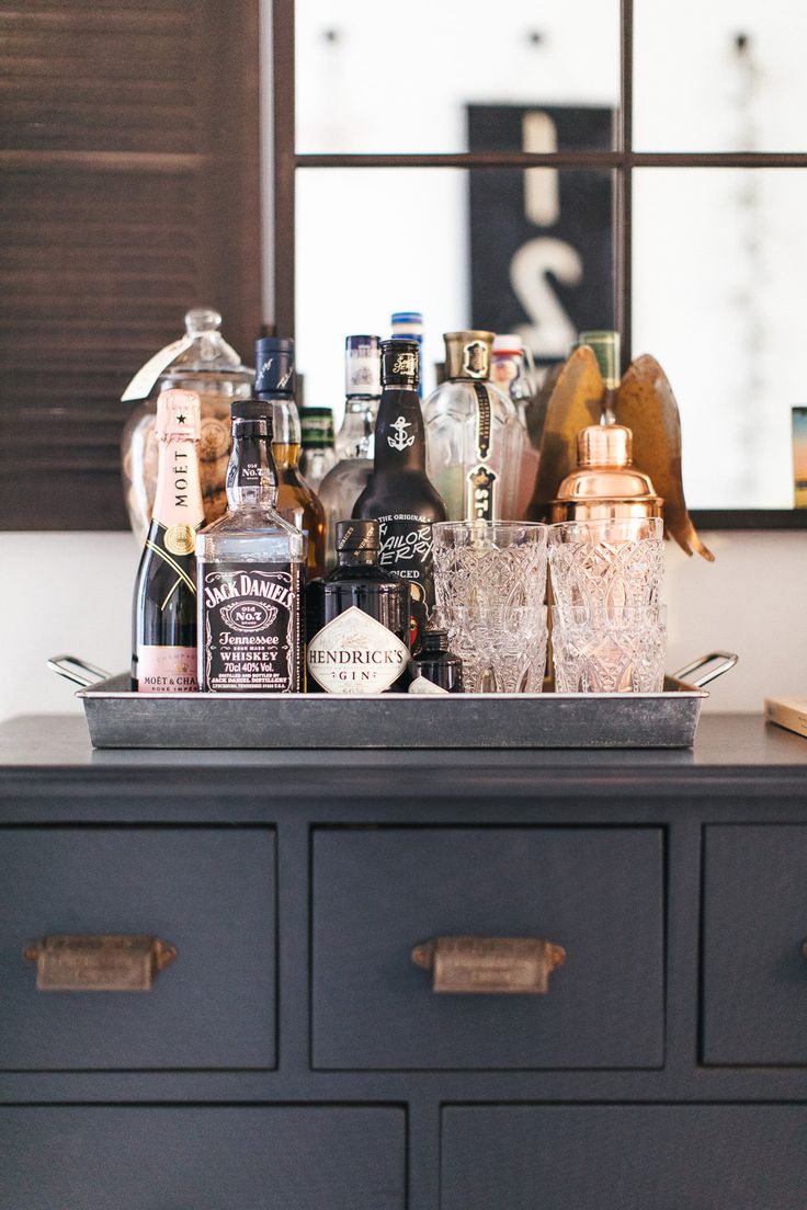 an assortment of liquor bottles and glasses on top of a dresser in front of a mirror