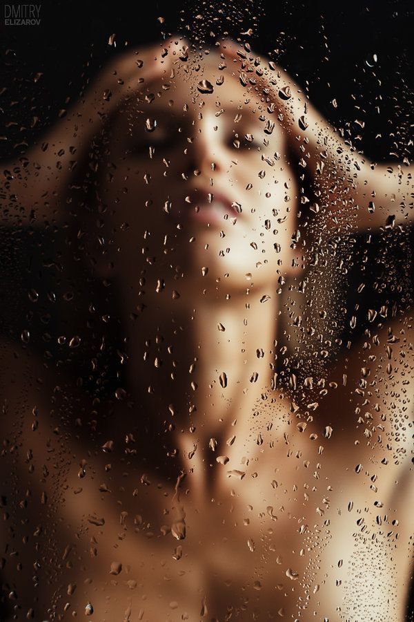 a woman standing in front of a window with rain drops on the glass and her hair blowing back