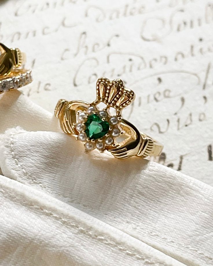 two gold rings with green and white stones on them sitting on top of a napkin