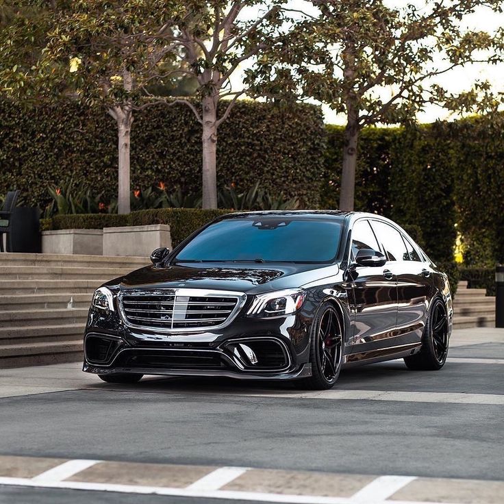 a black mercedes s - class parked in front of some steps and trees on the street