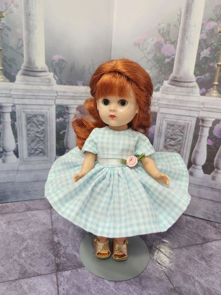 a doll with red hair wearing a blue and white checkered dress, standing on a pedestal