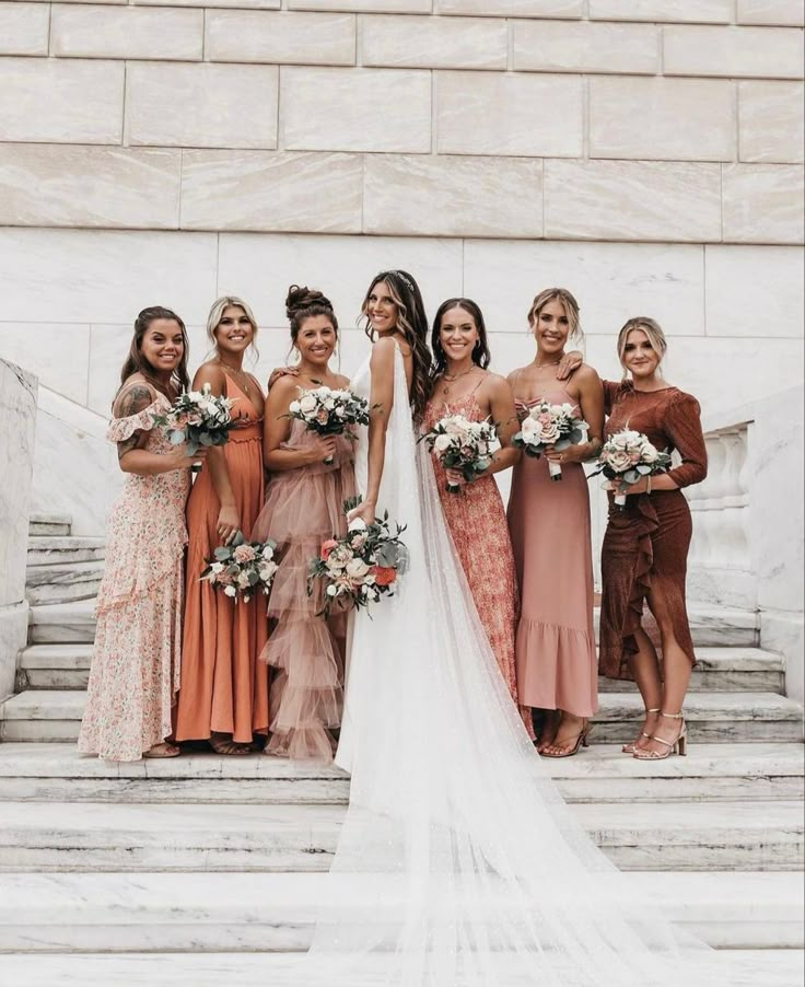 a group of women standing next to each other in front of a stone wall holding bouquets