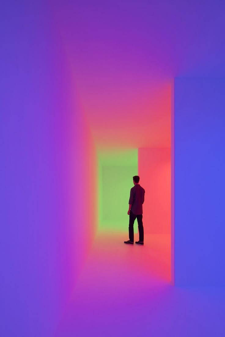 a man standing in an empty room with colored light coming from the ceiling and his back to the camera