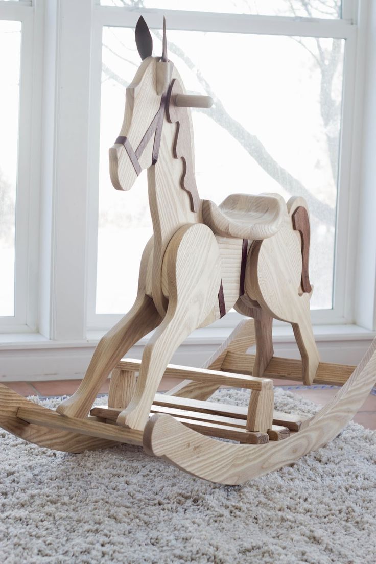 a wooden rocking horse sitting on top of a rug in front of a large window