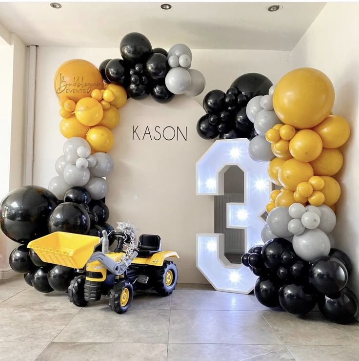 a room decorated with balloons and black and white balloons, including a yellow tractor parked in front of it