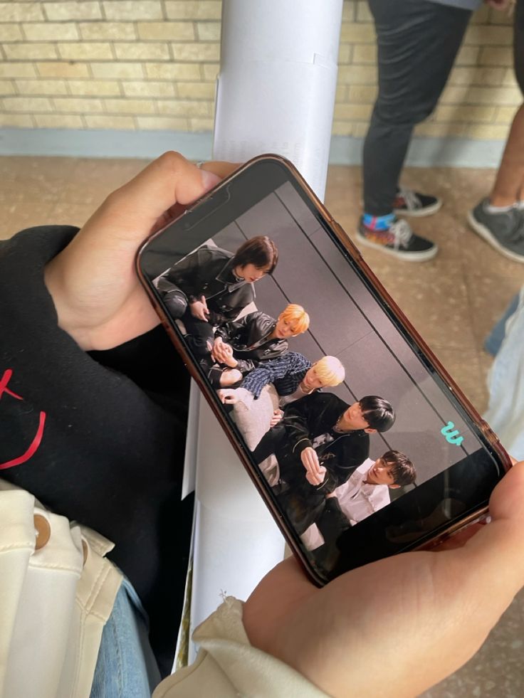 a person holding up a cell phone in front of a brick wall with other people standing around