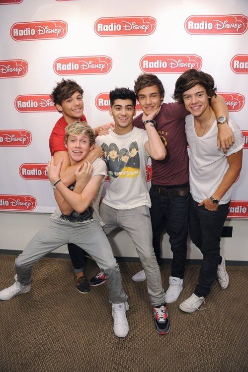 four young men posing for a photo in front of a radio disney logo wall with their arms around each other