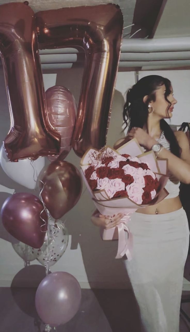 a woman holding a bouquet of roses in front of balloons and the number fifty sign