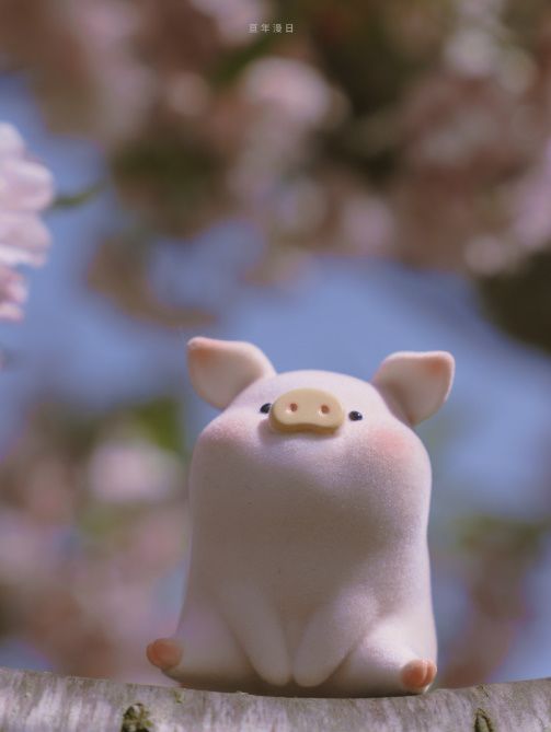 a small pig figurine sitting on top of a piece of wood with pink flowers in the background