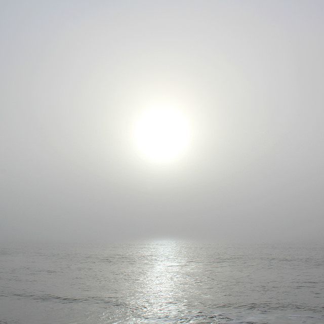 the sun is shining over the ocean on a foggy day with no one in it