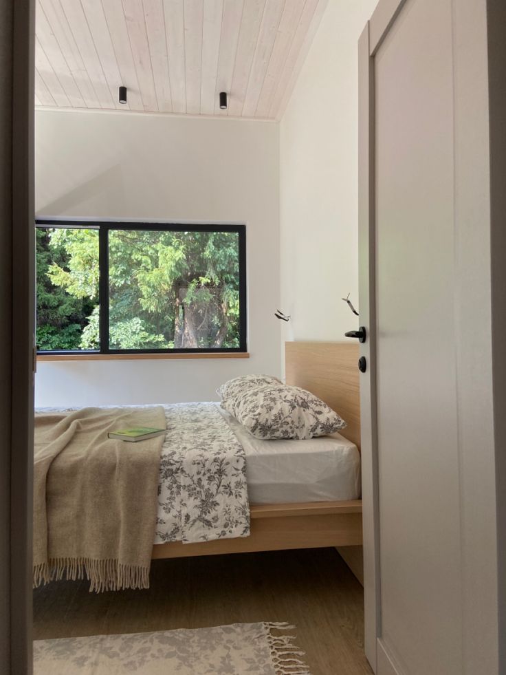 a bed sitting under a window in a bedroom next to a wooden floor and white walls