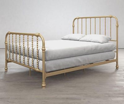 a gold metal bed frame with white sheets and pillows on the bottom, in an empty room