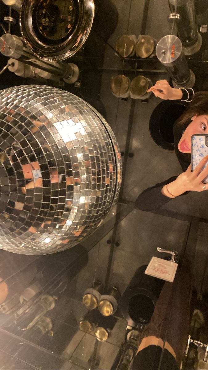 a woman taking a selfie with her cell phone in front of a disco ball