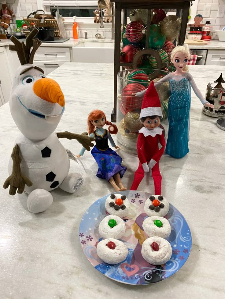 two elfs and three snowmen sitting on a kitchen counter with cupcakes in front of them