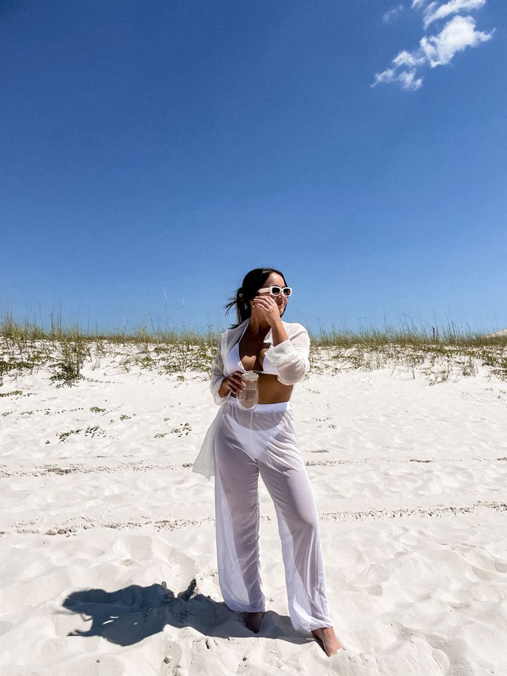 a woman standing on top of a sandy beach next to tall grass and blue sky